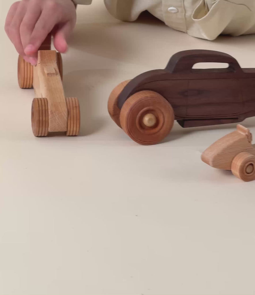A boy rolling a wooden race car on the ground. 