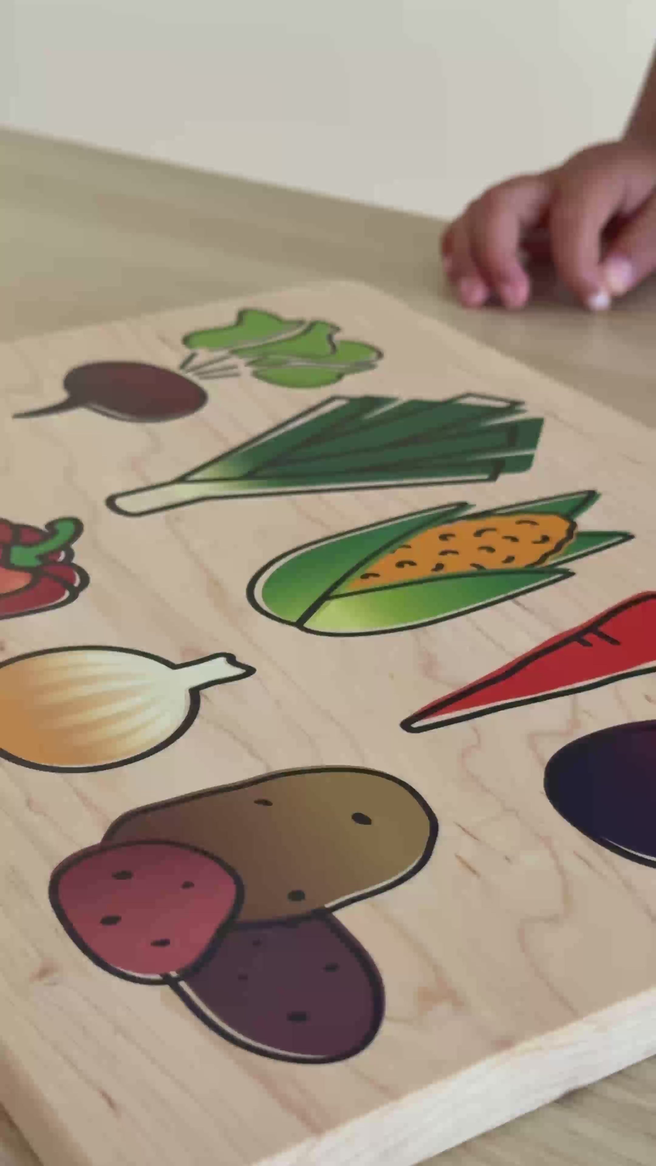 Little girl with a wooden cutting board and knife with veggies printed on it.