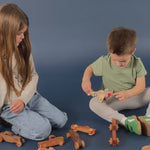 A brother and sister sitting on the floor playing with P-51 Mustang wooden airplanes and wooden trucks.