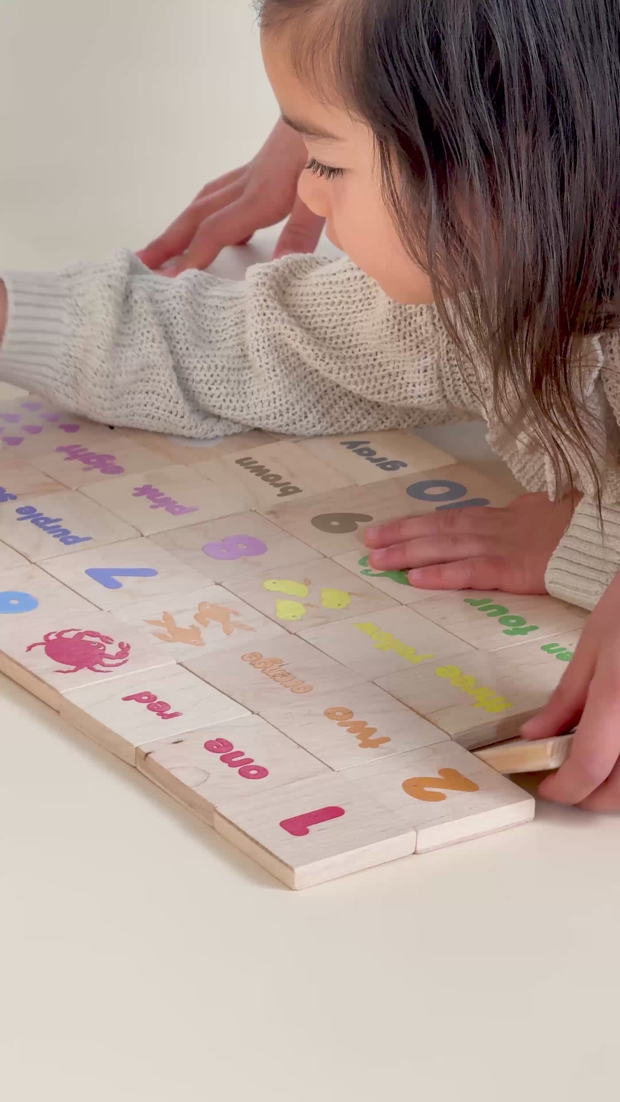 A little girl and her brother playing with Montessori inspired learning tiles with numerals, symbols and colors.
